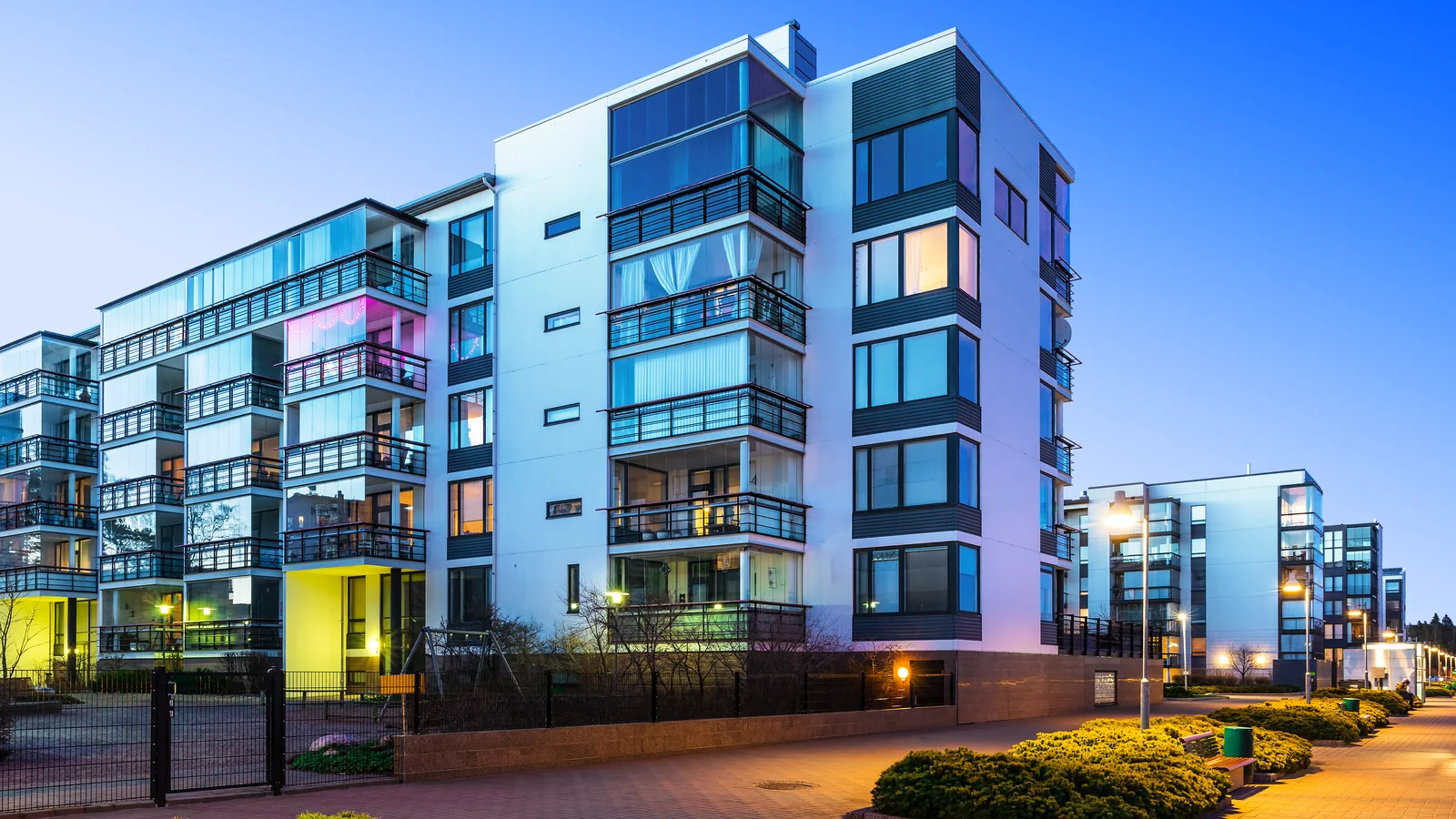 A modern multifamily building at dusk: cladding, glazing, balcony waterproofing and the transitions between them.