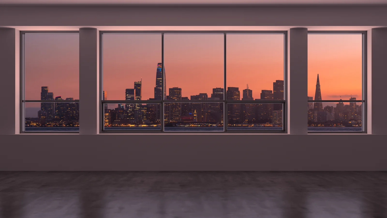 An empty floor behind a full-height curtain wall at dusk, looking out over a city skyline.