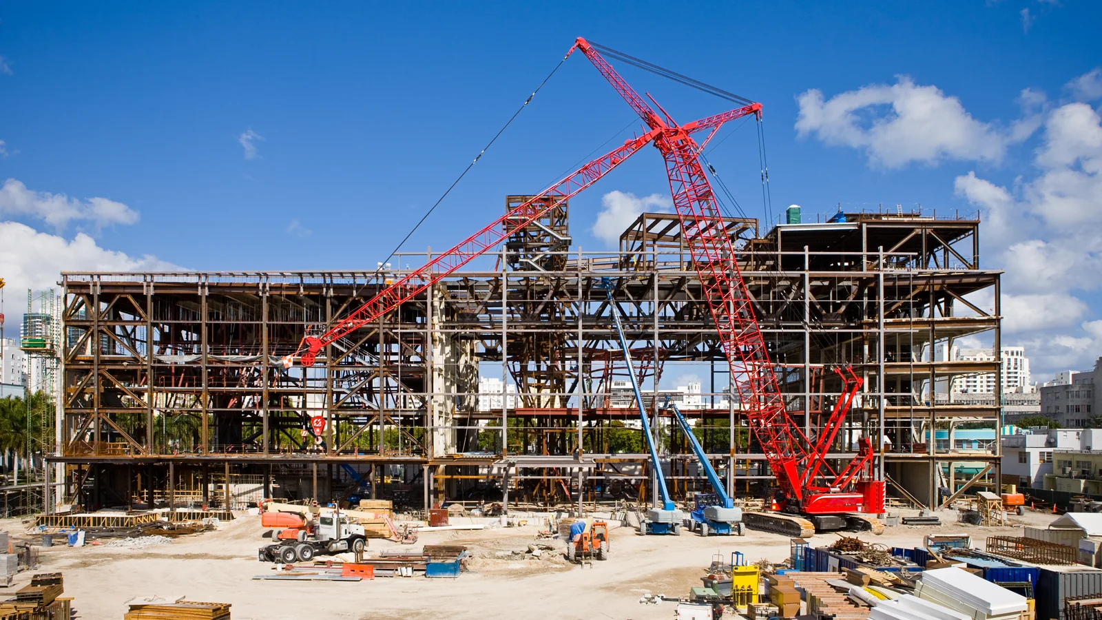 A steel frame going up on an urban site, with the crawler crane still standing inside the structure.